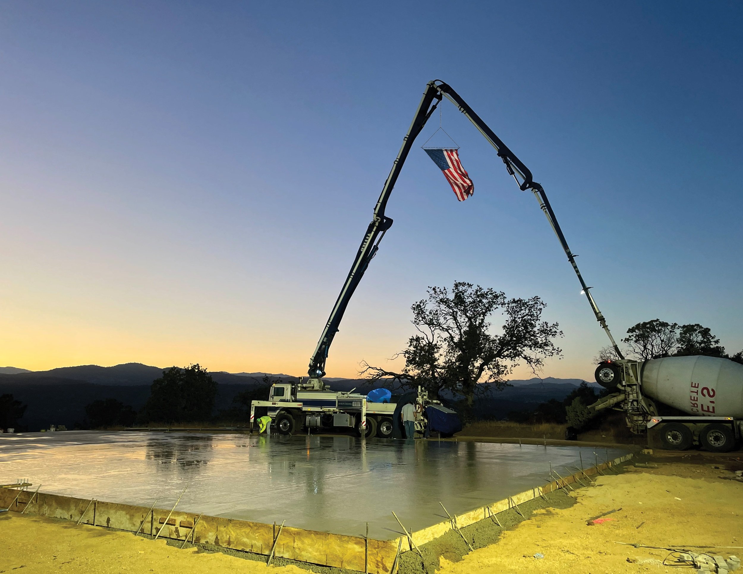 American flag on concrete pump truck boom at sunset during commercial slab pour — Liaison Concrete Construction