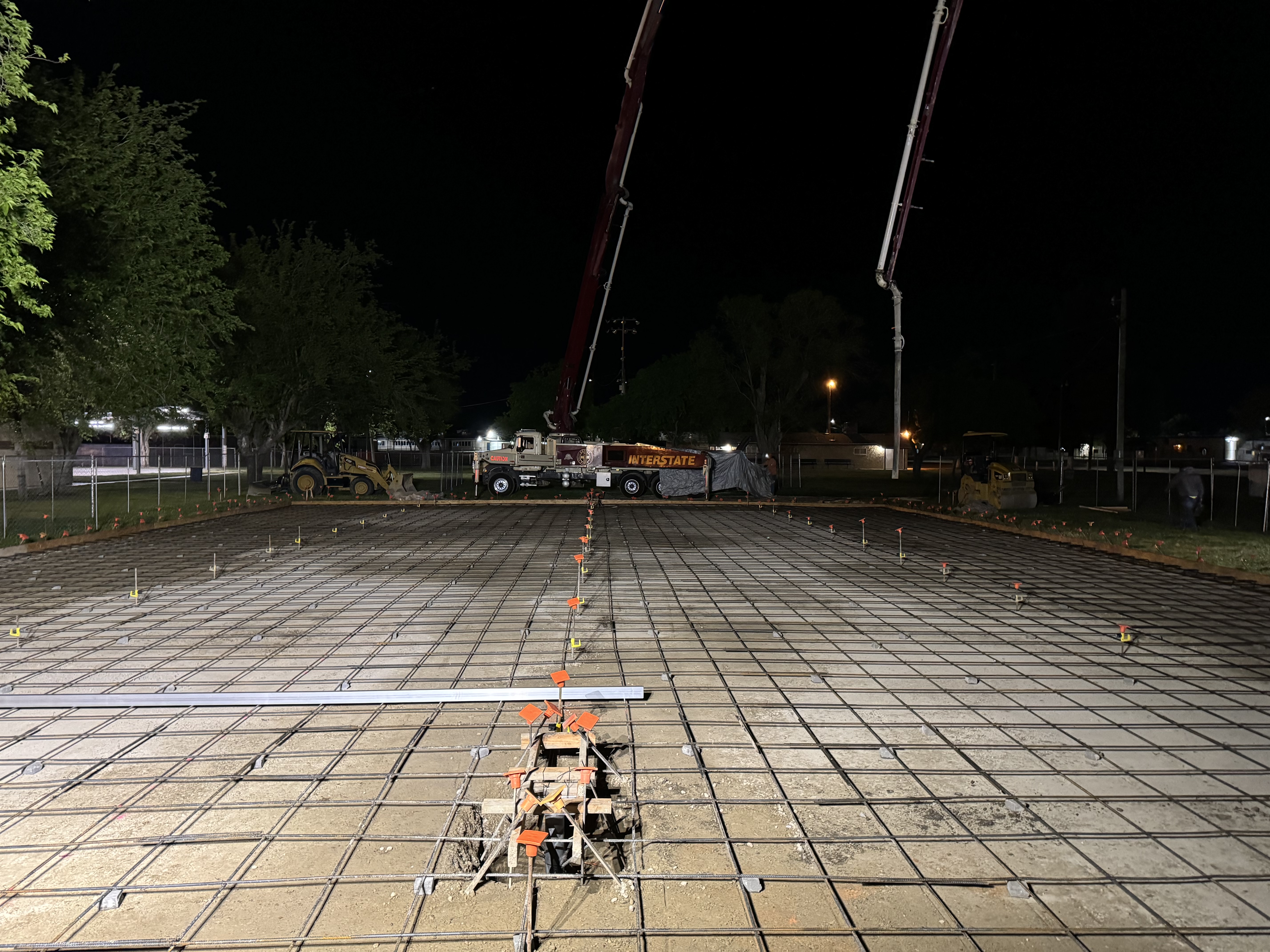 Concrete pump truck and laser screed over rebar grid at night on commercial slab project