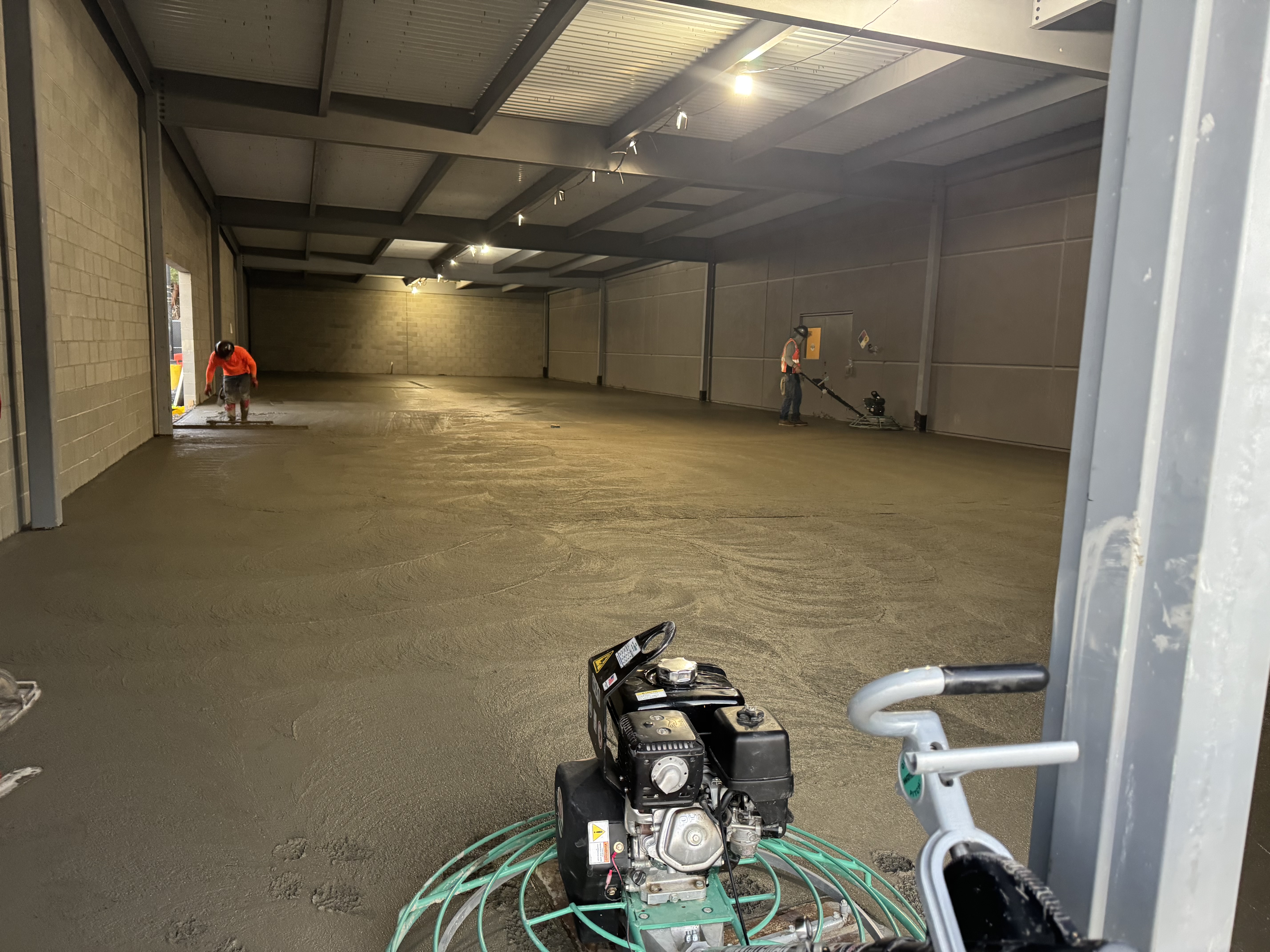 Crew finishing concrete floor inside commercial warehouse with power trowels