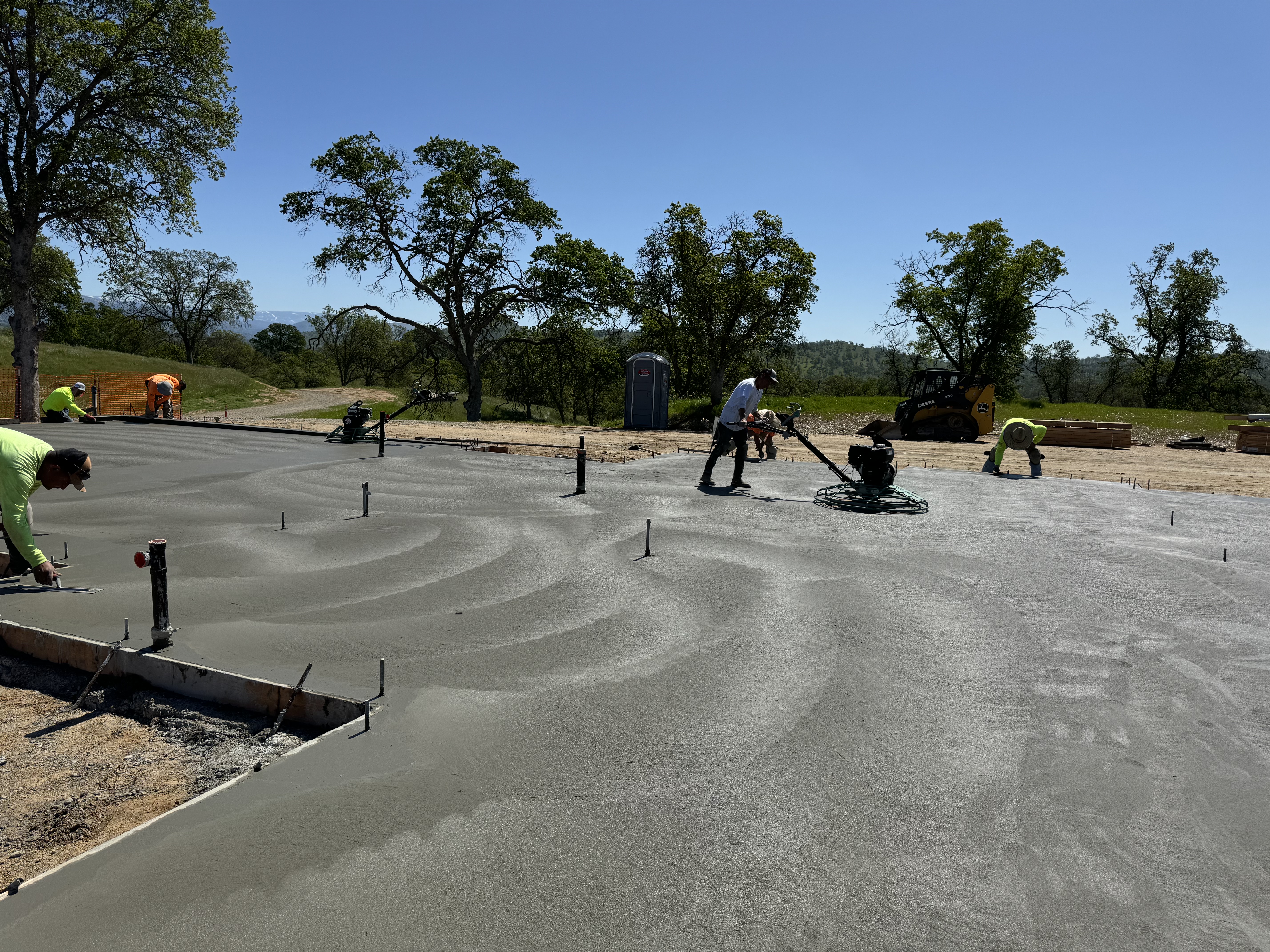Crew power-troweling freshly placed concrete slab with oak trees in background, Northern California
