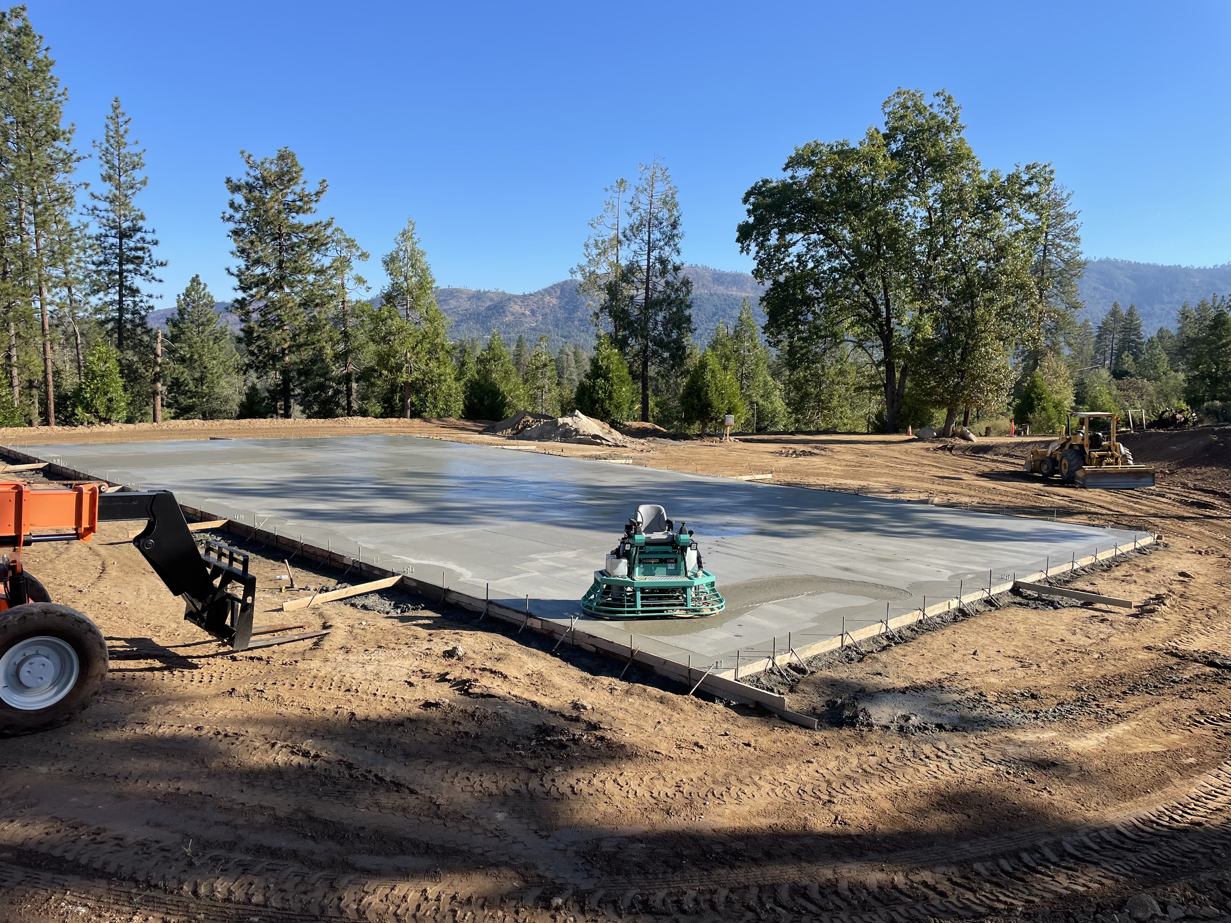 Power trowel finishing large concrete slab with mountains in background on commercial project