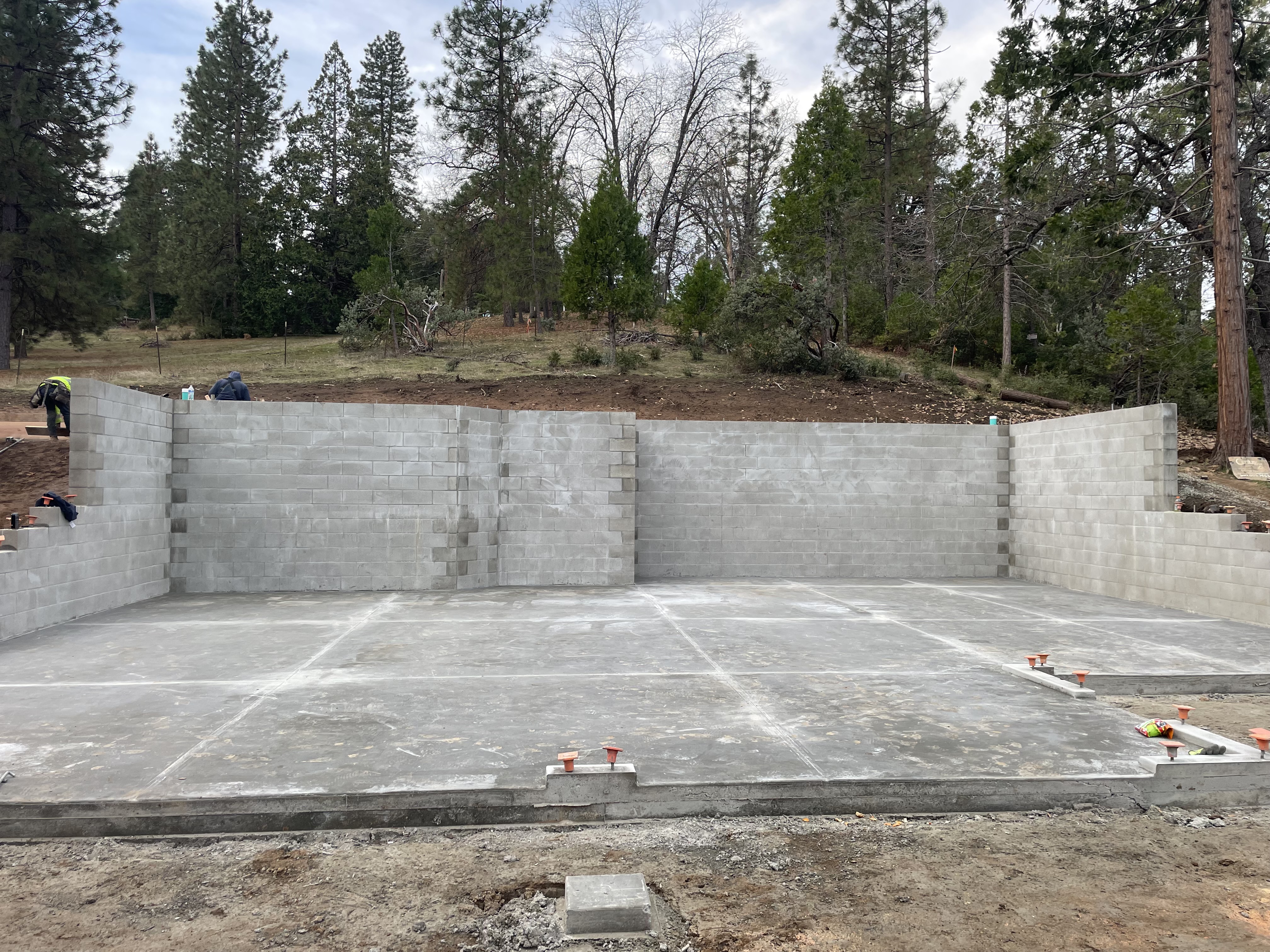 Completed CMU concrete block retaining walls with fresh slab, forested Northern California setting