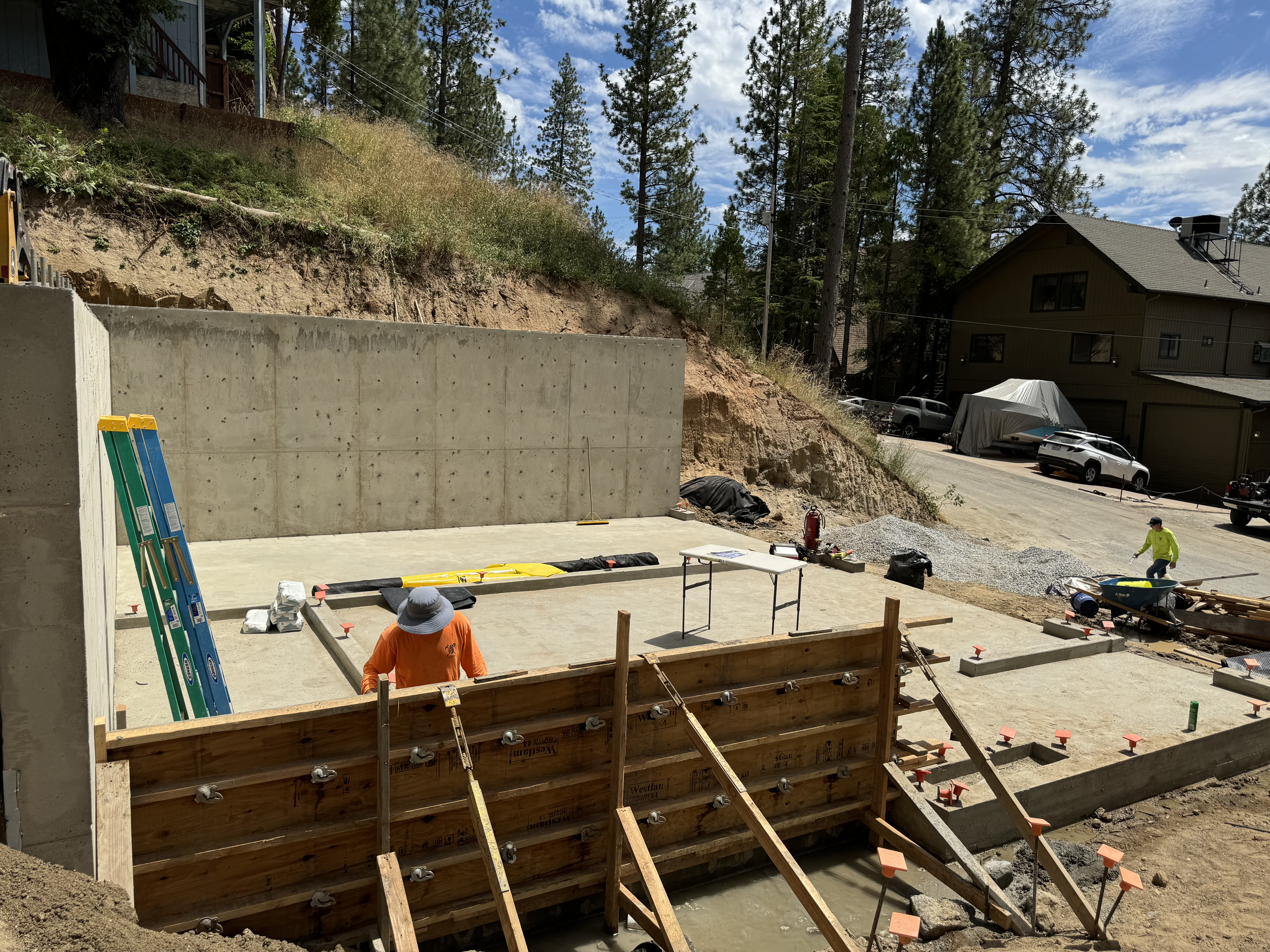 Completed concrete retaining wall next to fresh slab prep in mountain setting, Northern California