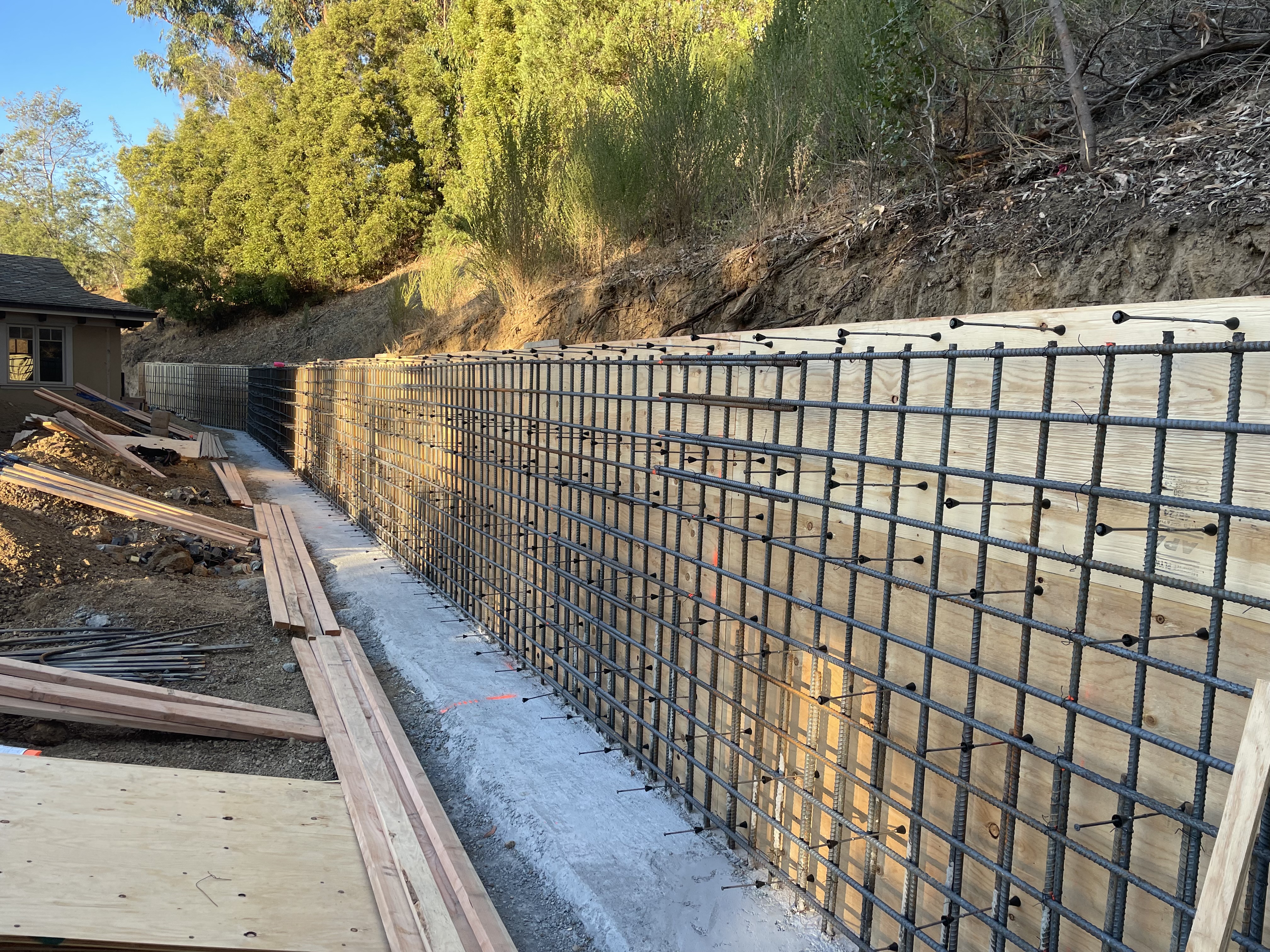 Engineered retaining wall rebar cage with hillside backdrop on commercial site
