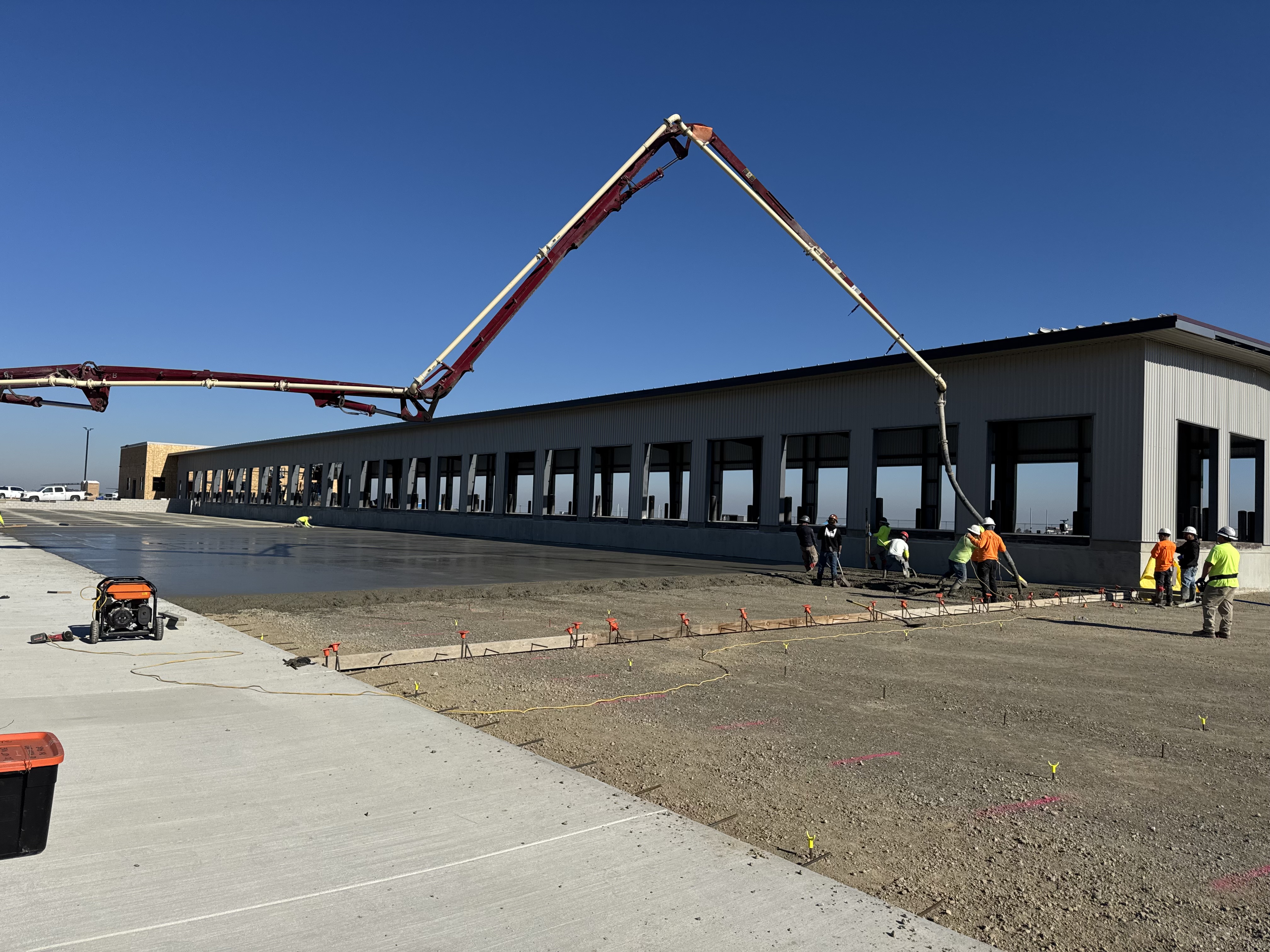 Wide shot of pump truck placing concrete slab at commercial warehouse with loading docks, Northern California